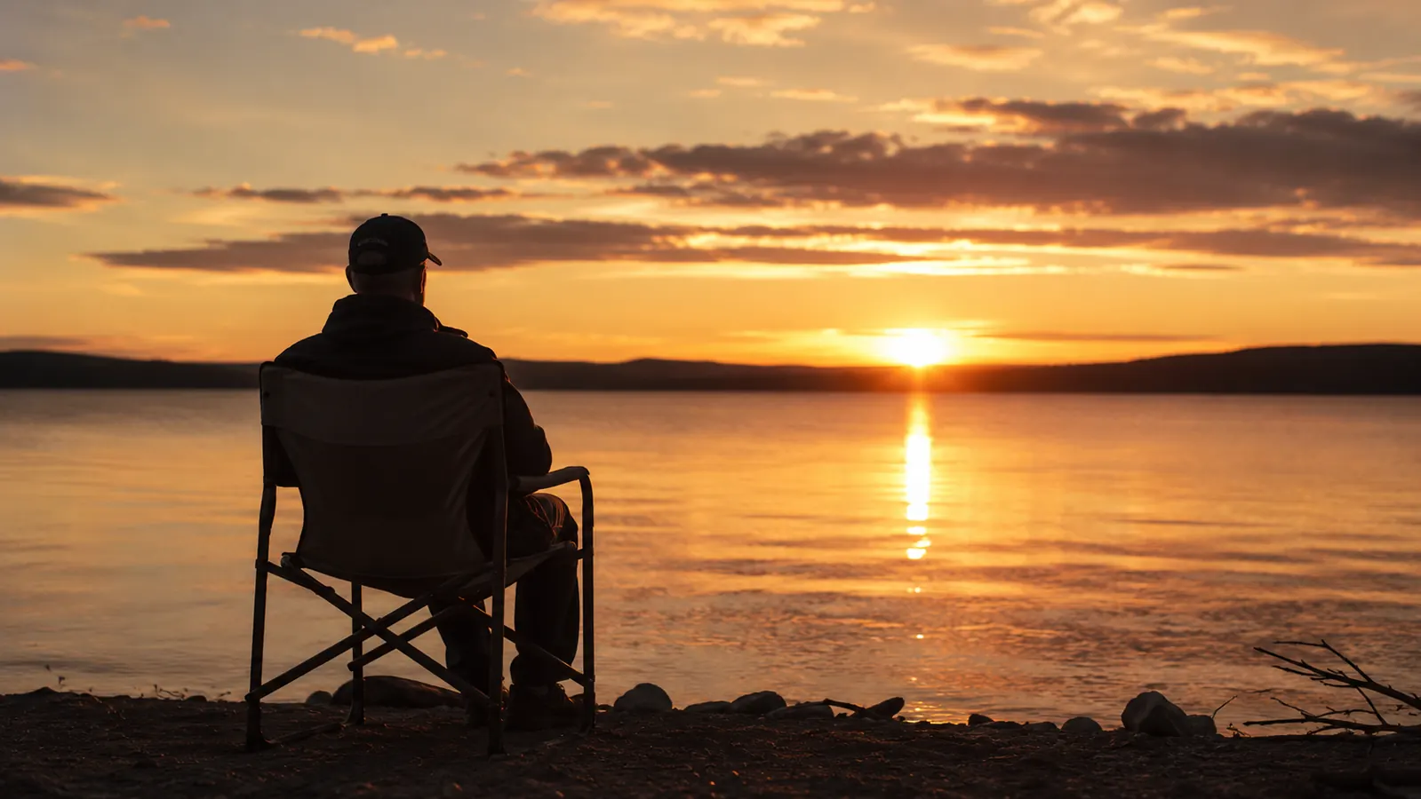 Camping chair set up at the edge of a lake at dusk with a person watching the sunset
