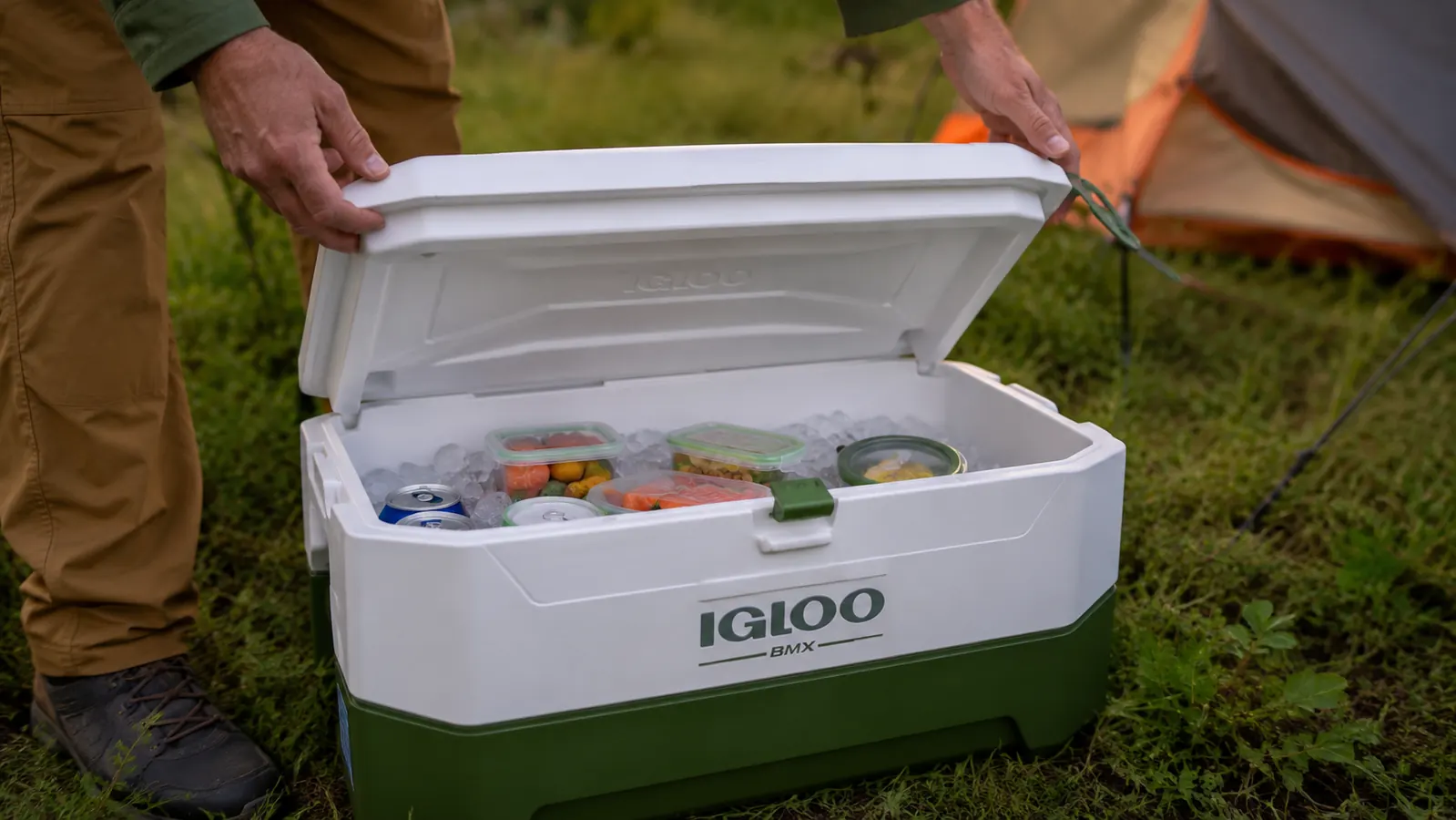 Hand opening the lid of an Igloo BMX cooler revealing ice and organized food containers inside
