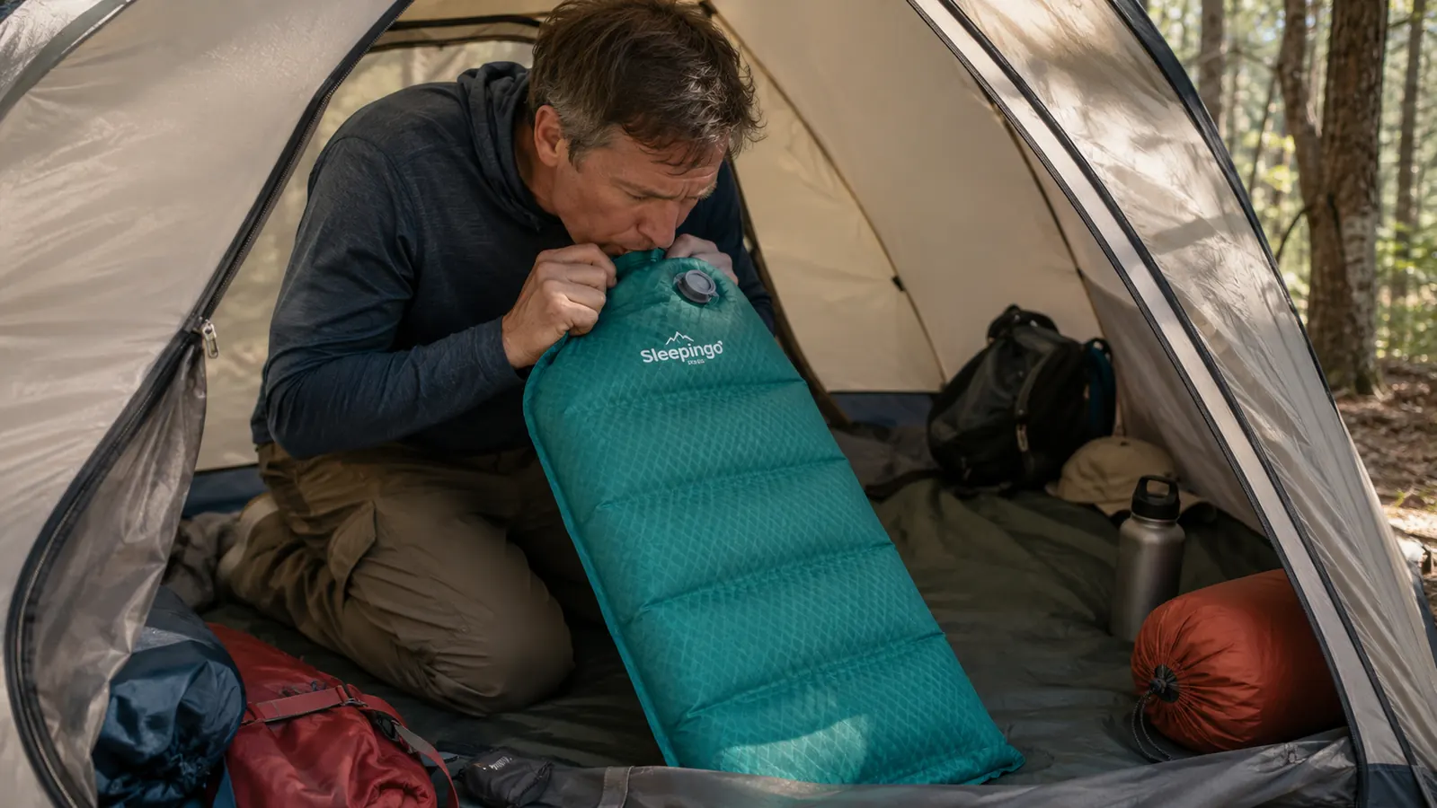Camper unrolling and inflating a Sleepingo sleeping pad inside a backpacking tent