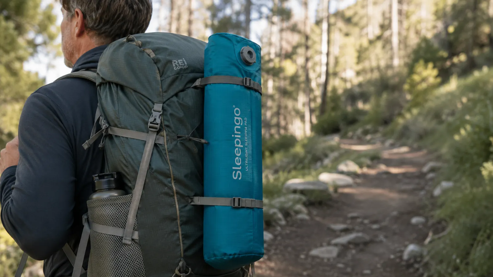 Rolled-up Sleepingo sleeping pad next to a packed backpack showing compact size