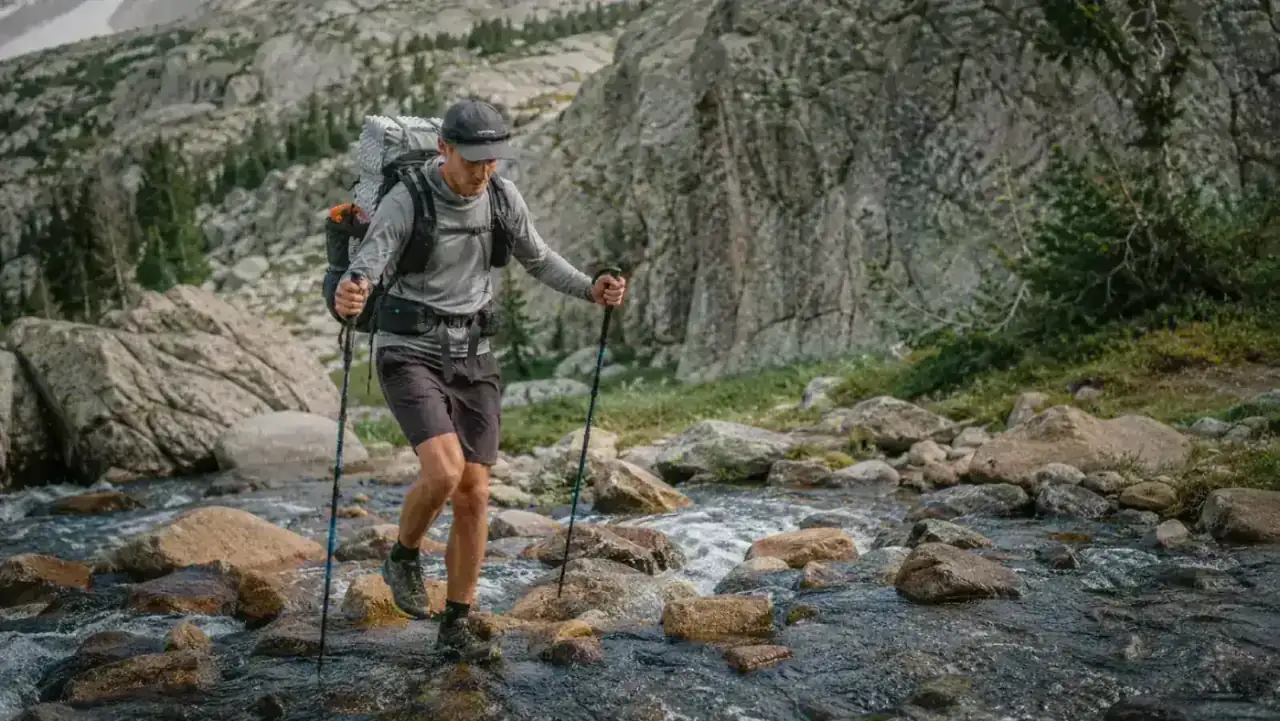 Hiker with ultralight pack preparing to cross a mountain stream, showing backpacking gear priorities