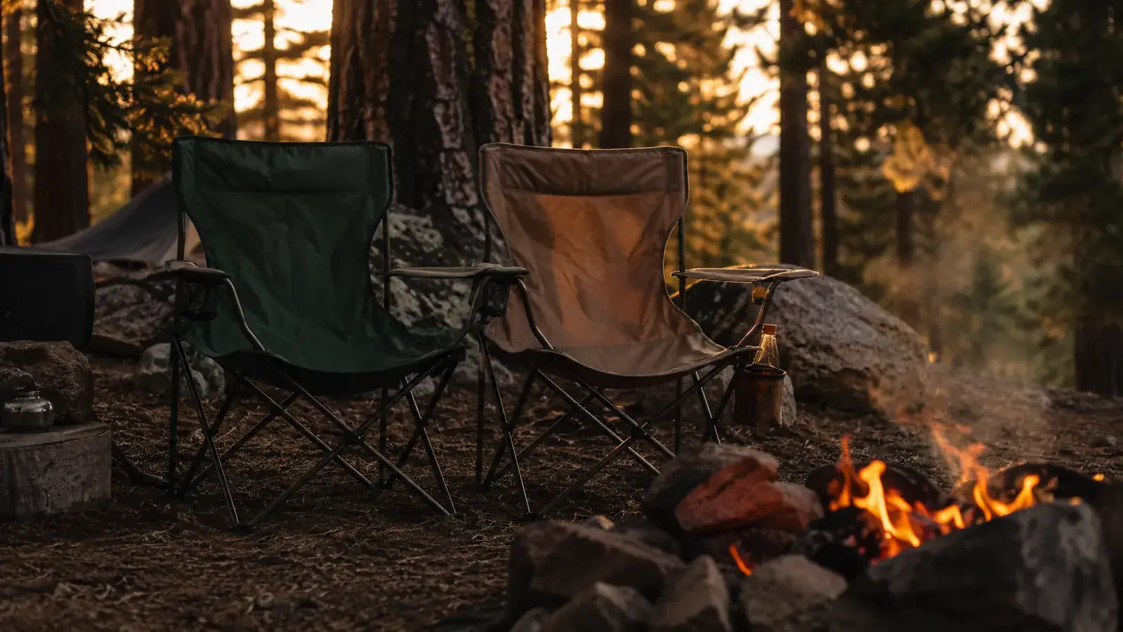 Two camp chairs side by side at a forested campsite at dusk, one a classic folding chair and one a sleek ultralight chair