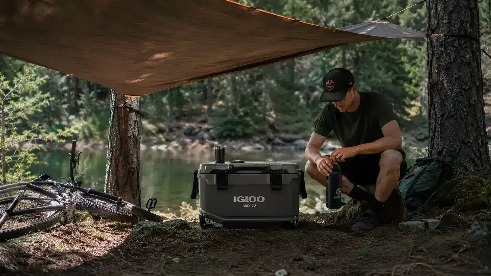 Igloo BMX cooler in the shade under a tarp at a campsite with trees around