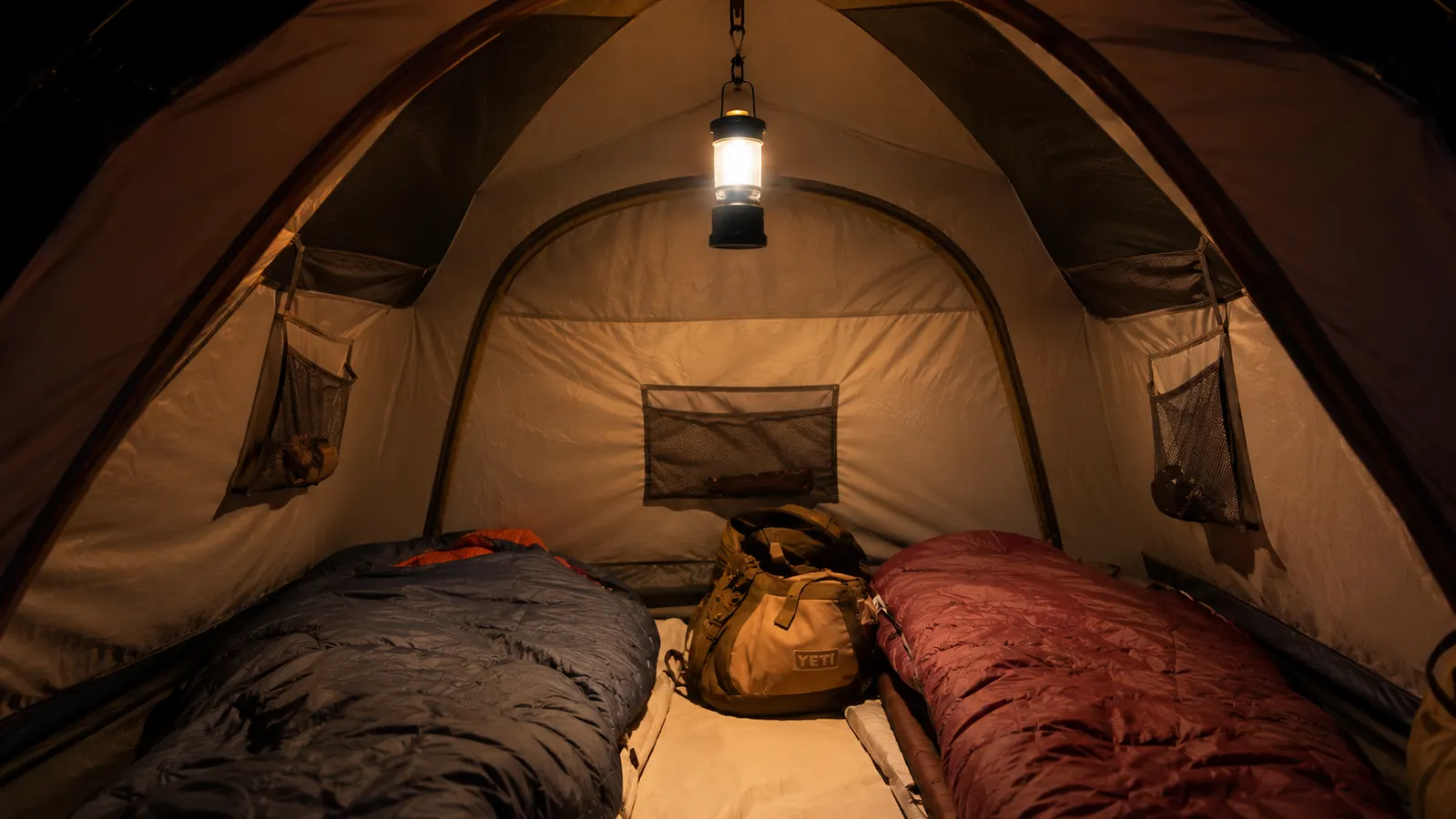 Lepro lantern hanging from a tent loop at night inside a dome tent casting even light across sleeping bags