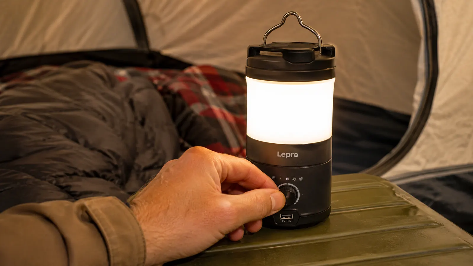 Hand adjusting the brightness dial on the Lepro camping lantern while it illuminates a tent interior