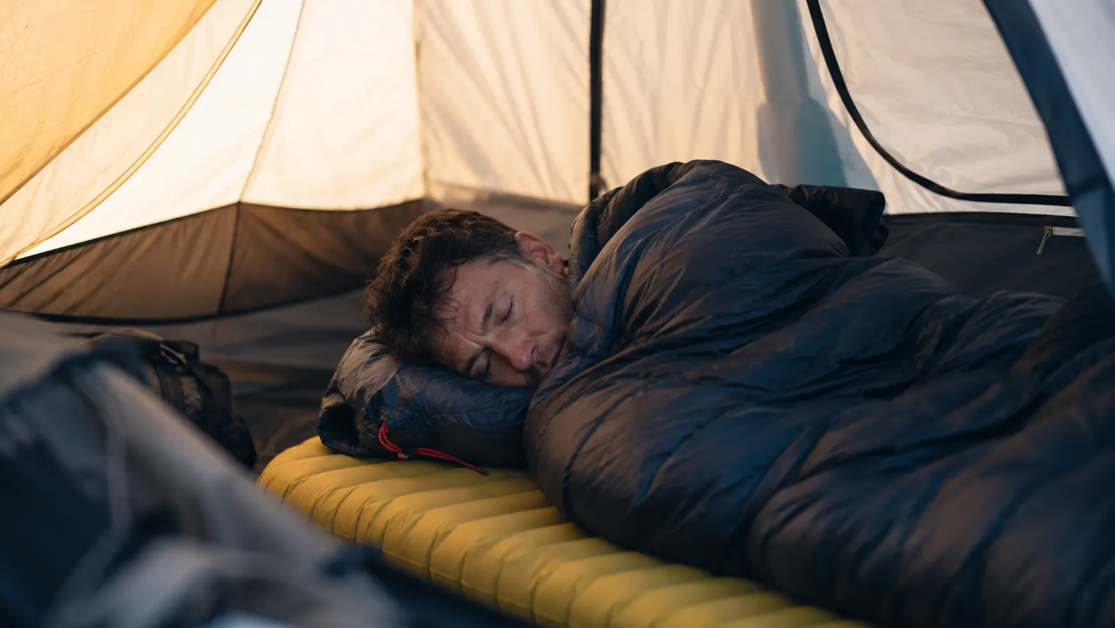 Camper sleeping soundly in a sleeping bag on an inflated pad inside a tent