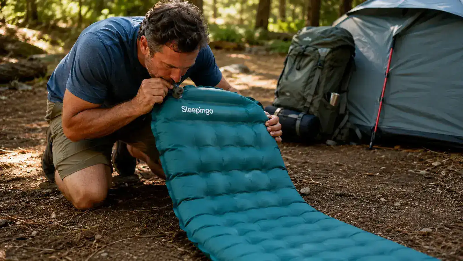 Person blowing into the valve of a Sleepingo sleeping pad to inflate it at a campsite